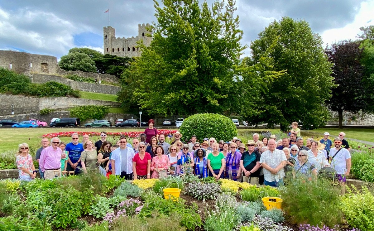 Around 50 volunteers and guests pose in front of the Sensory Garden, with Rochester Castle in the background
